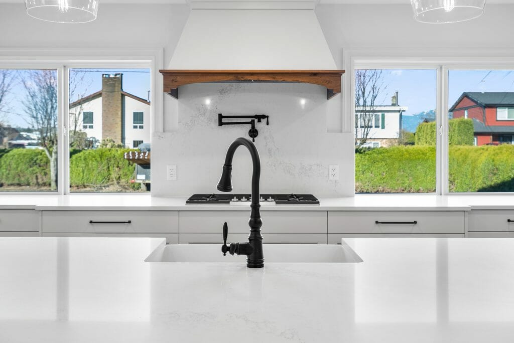 View from behind the kitchen sink showing gas stove, cabinets and kitchen windows