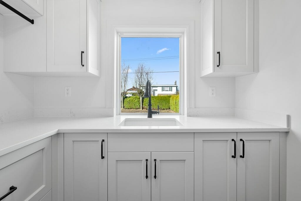 Newly installed white laundry room cabinets with a window behind the sink.
