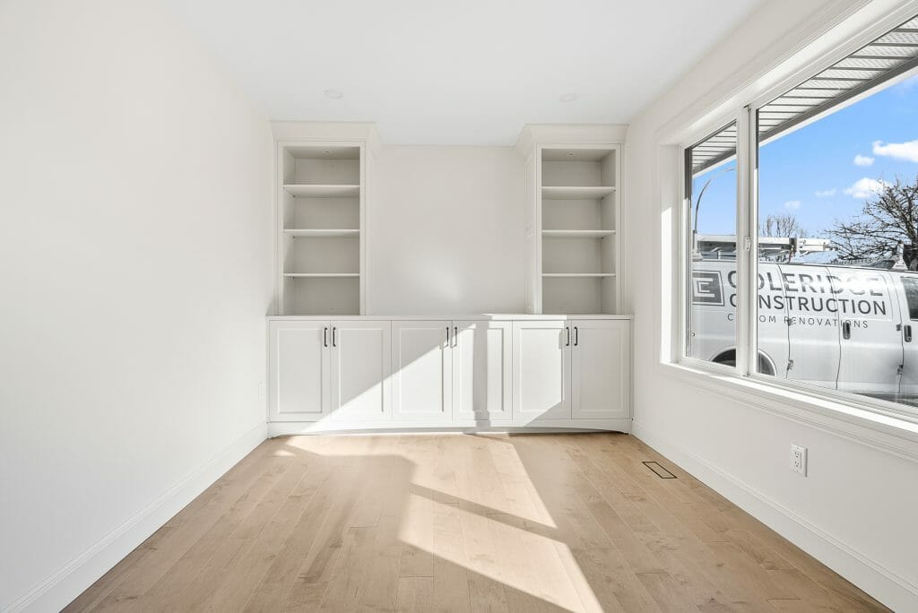 A bright room with laminate flooring, a very large window, and built-in cabinets and bookshelf.